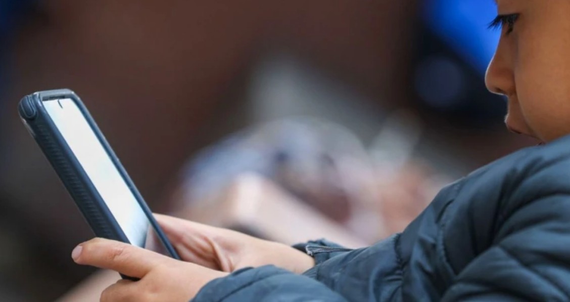Adolescente usando un teléfono celular mientras navega en redes sociales.