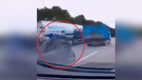 Motociclista casi muere aplastado por un tráiler tras caerle una la lona en la cara (Vídeo)